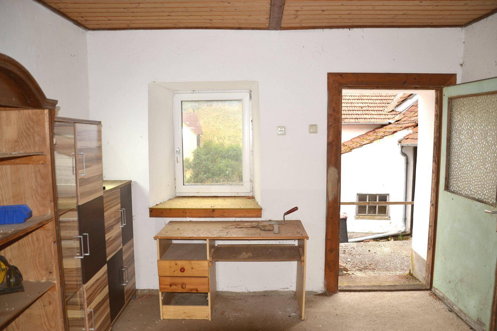 Einfacher Raum mit Holzbalkendecke, einem Schreibtisch und Blick auf den Hof.