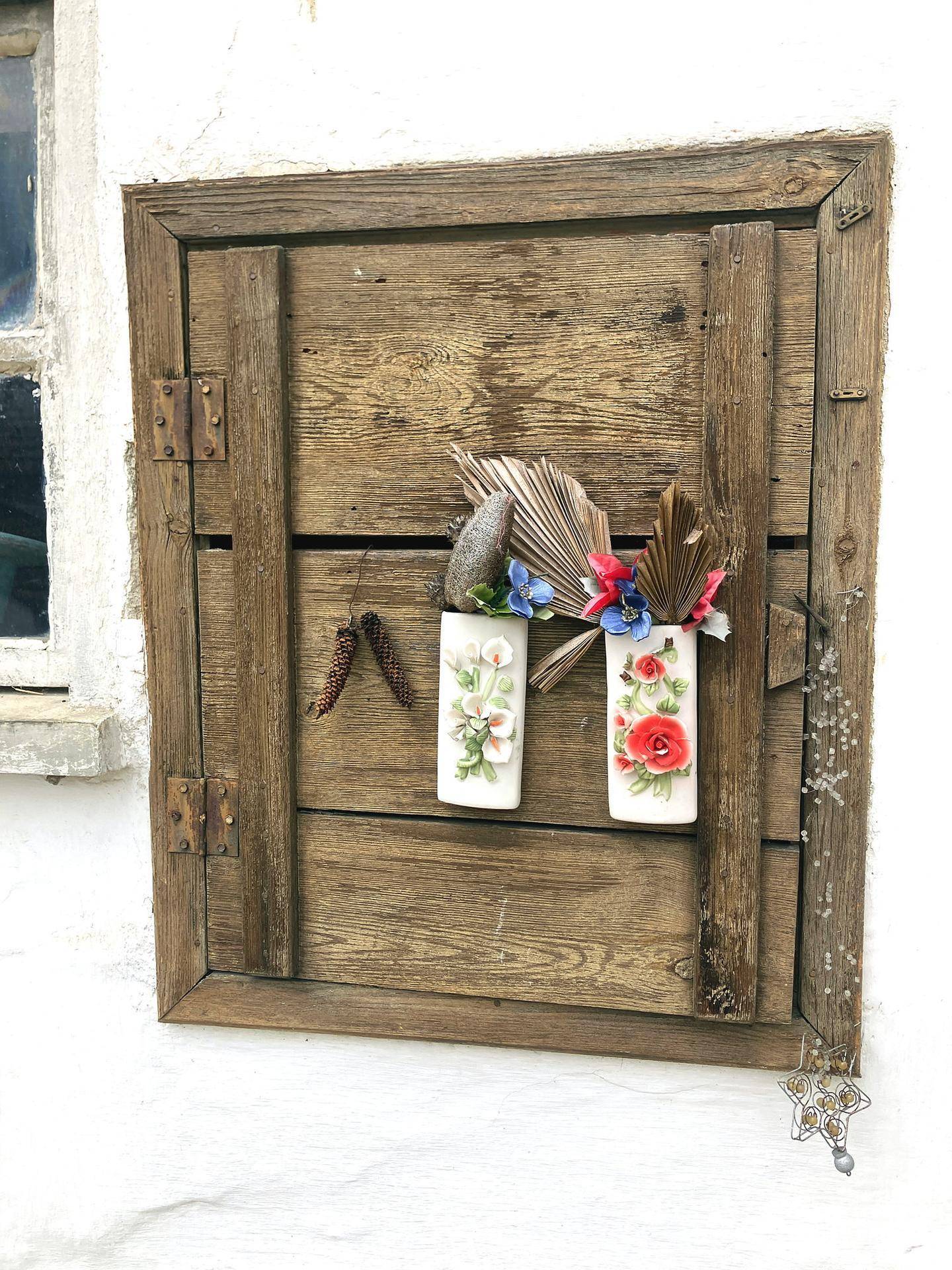 Rustikale Holzfensterläden mit dekorativen Blumenvasen an einer weißen Hauswand.