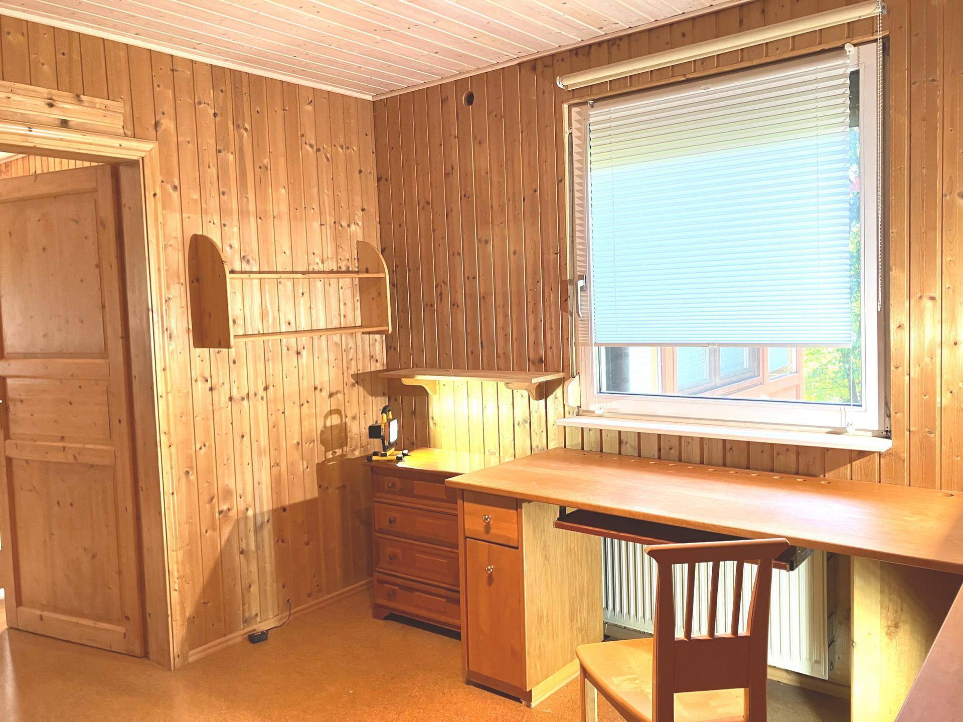 Helles Arbeitszimmer mit Holzvertäfelung, Schreibtisch und Fenster mit Jalousien.