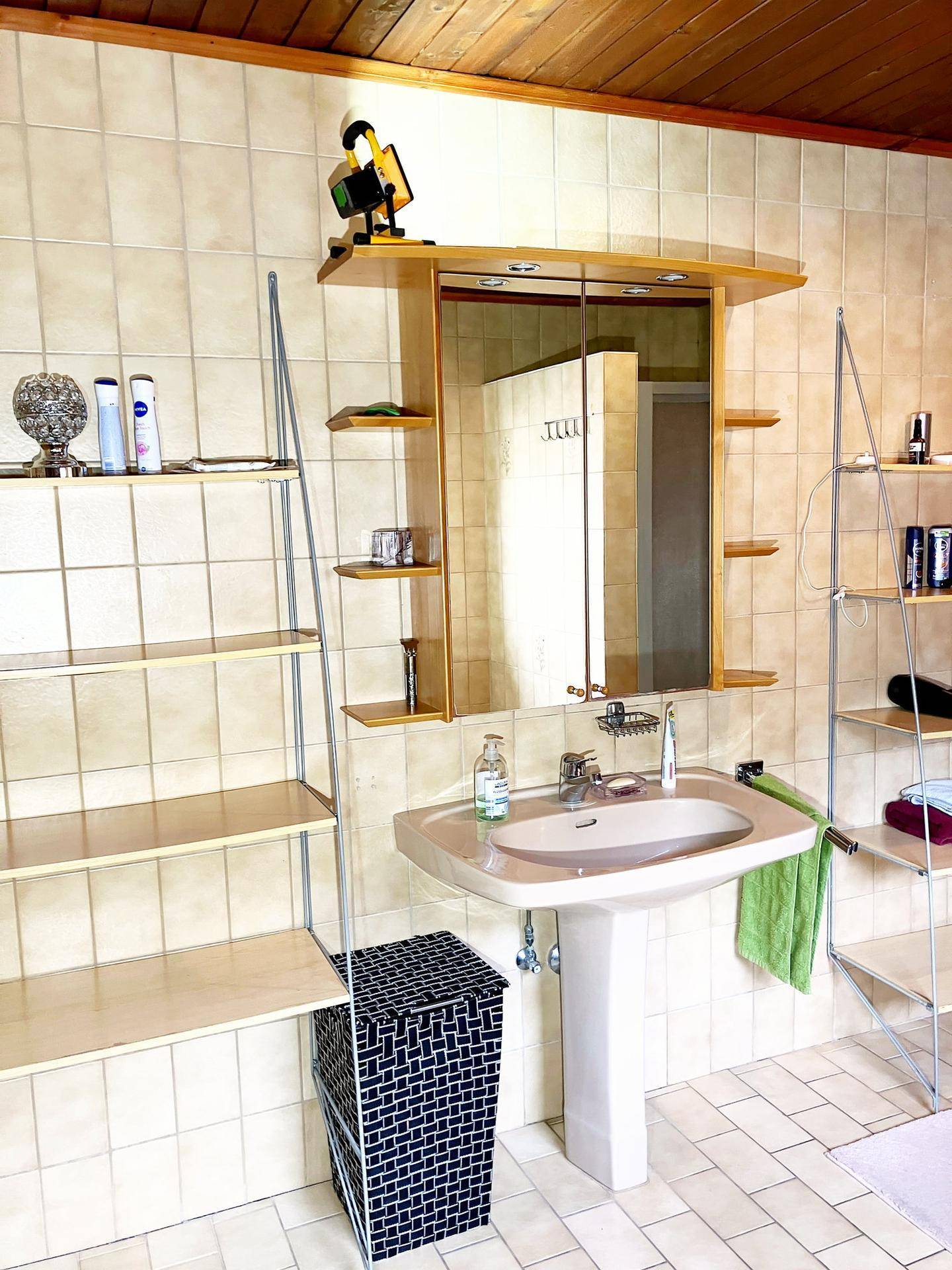 Badezimmer mit Standwaschbecken, Spiegelschrank und beigefarbenen Fliesen.