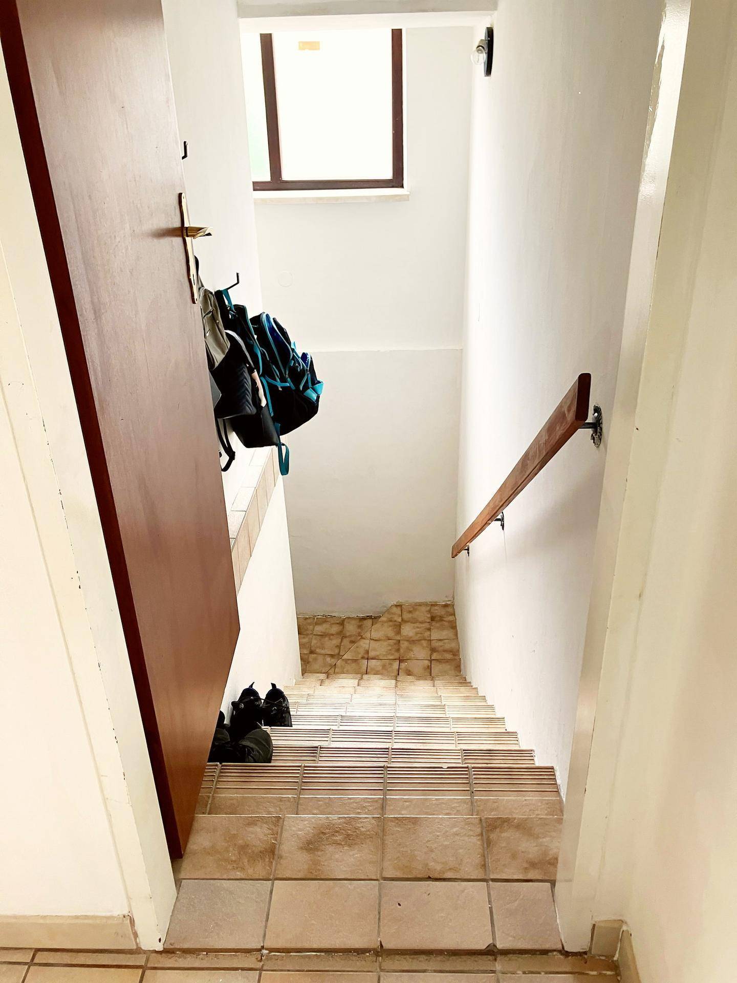 Treppenhaus mit gefliesten Stufen, Holzgeländer und weiß gestrichenen Wänden, führt in ein Obergeschoss.