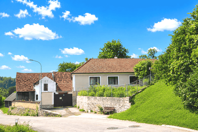 Hausansicht mit Garten und ländlicher Umgebung unter blauem Himmel.