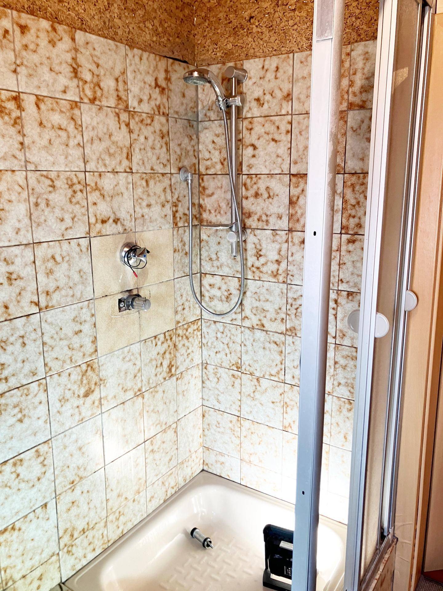 Duschbereich in einem Badezimmer mit braun-beigen Fliesen und Duschkabine.