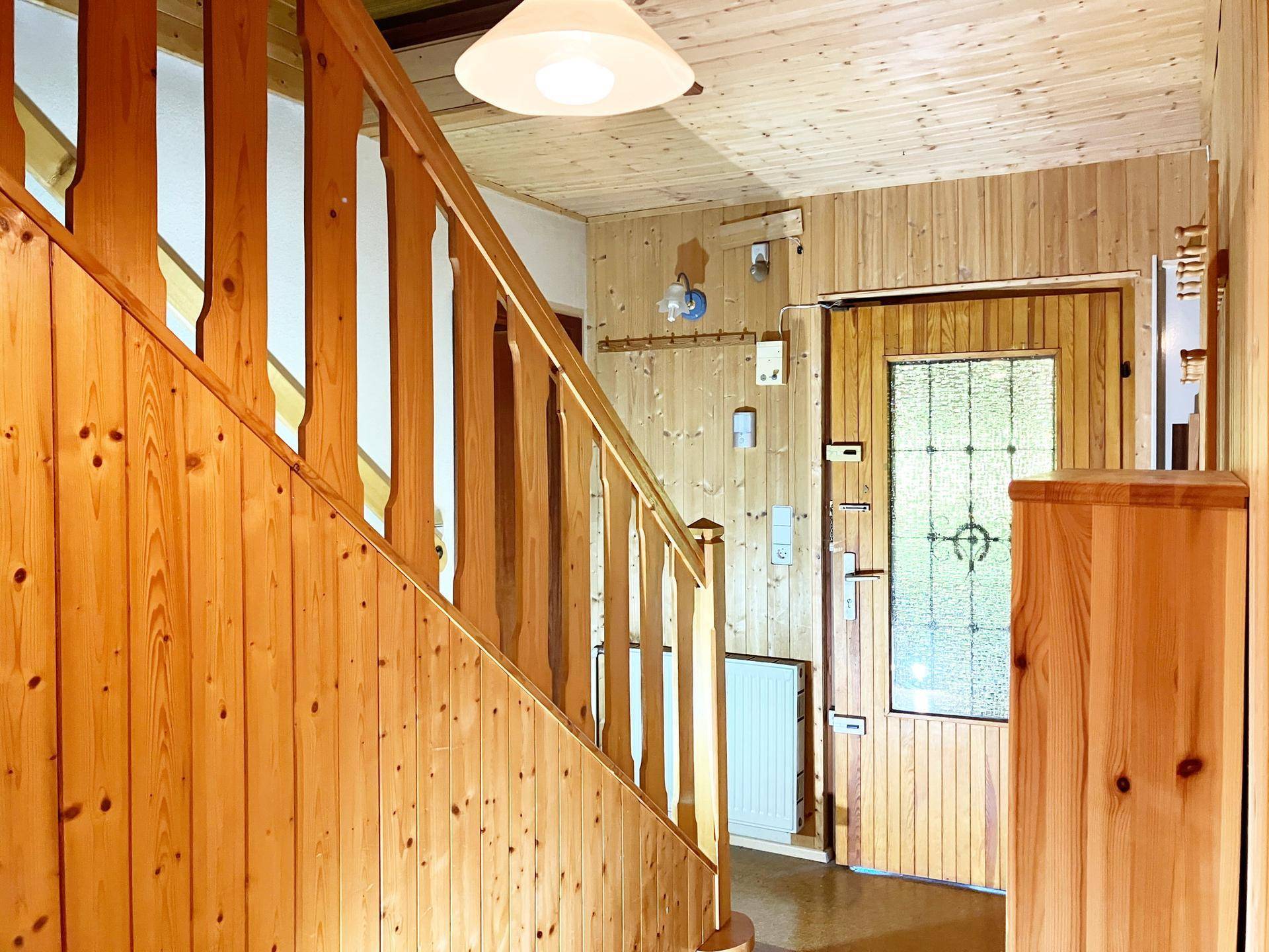 Eingangsbereich mit Holztreppe und Holzvertäfelung, die zum Obergeschoss führt.