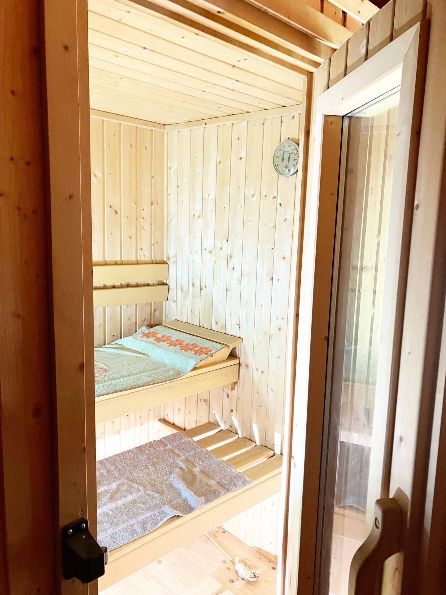 Innenansicht einer Holzsauna mit zwei Bänken und einem Thermometer an der Wand.