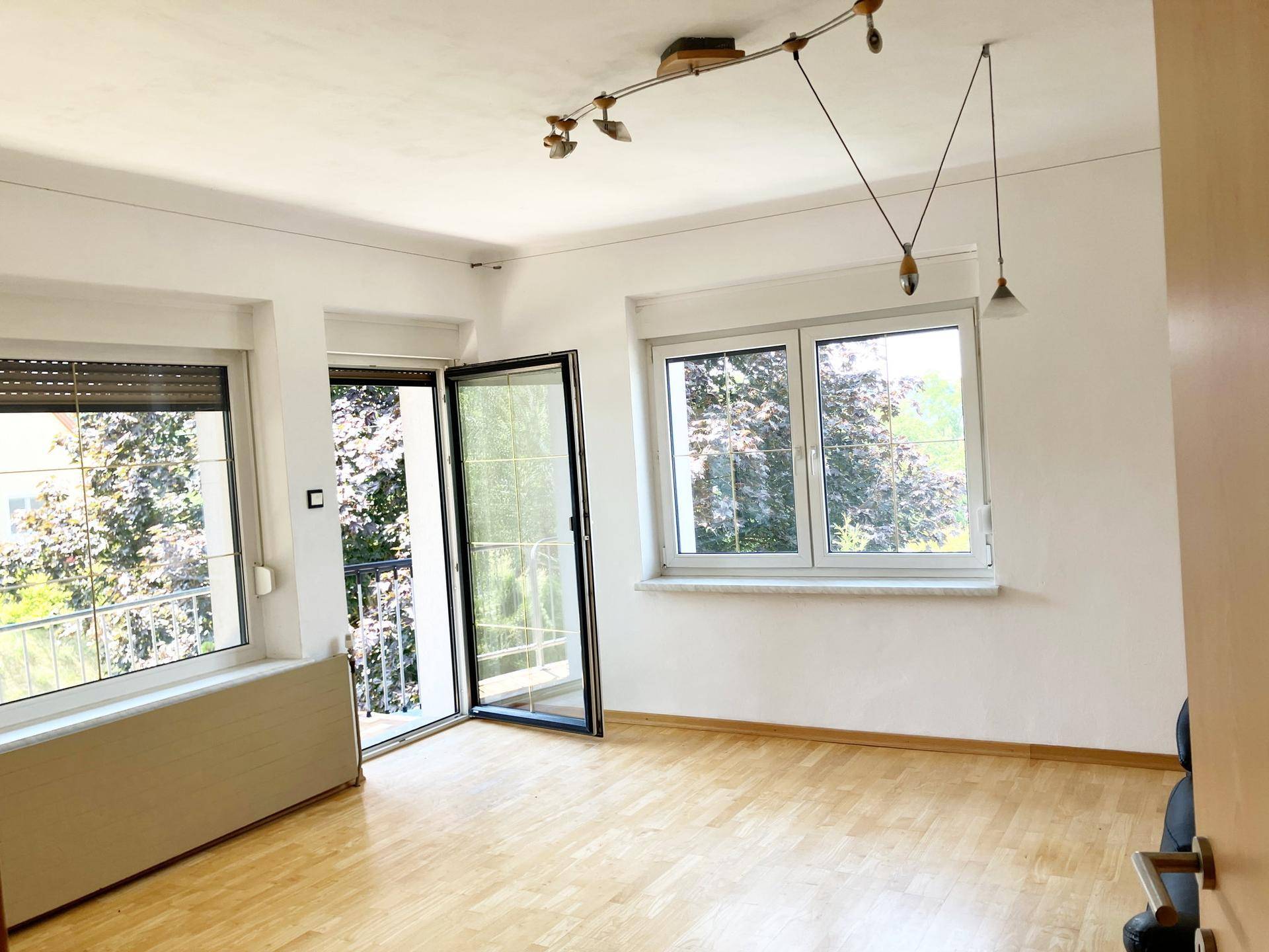 Helles Wohnzimmer mit Holzboden, großem Fenster und direktem Zugang zum Balkon.