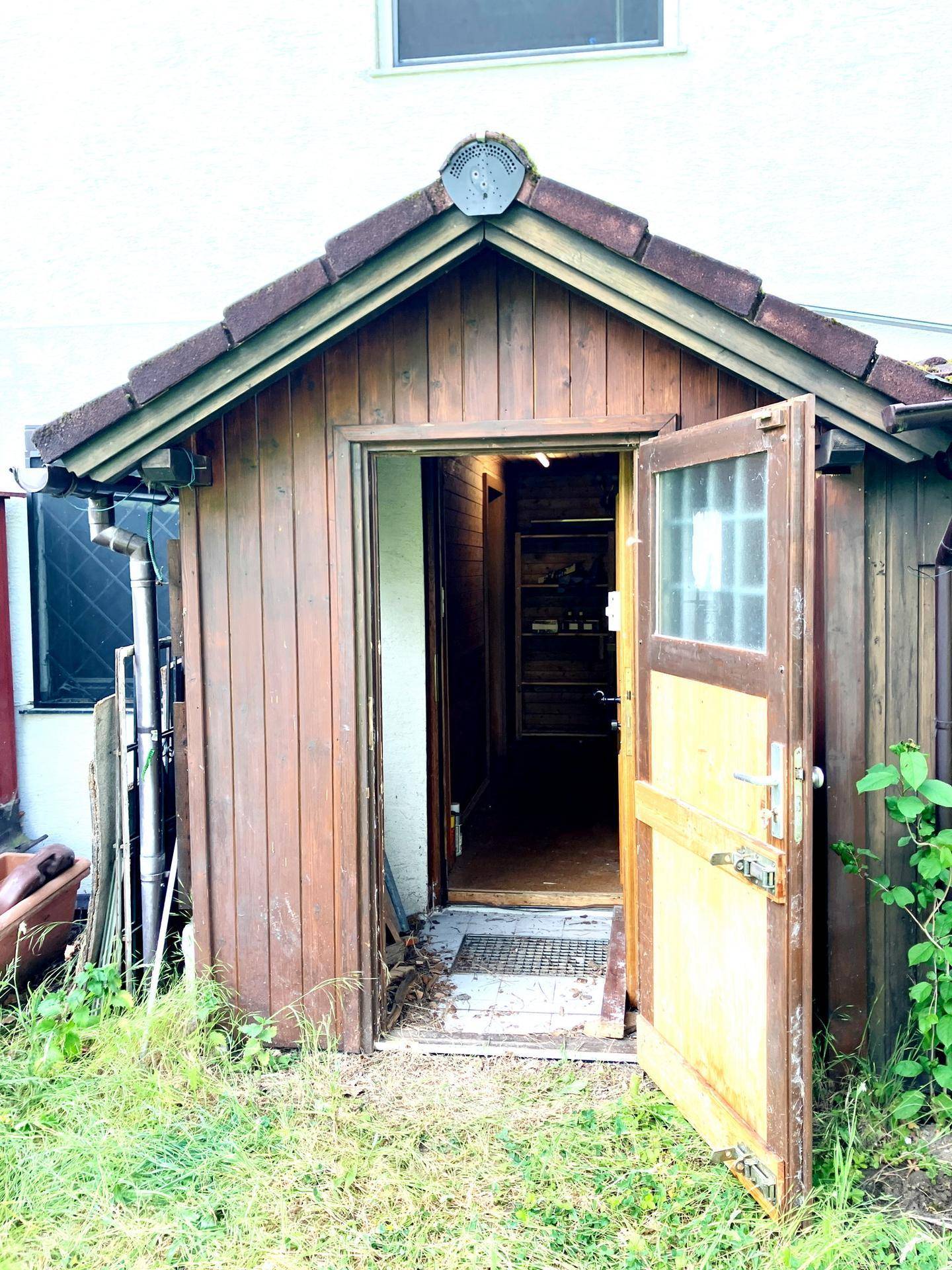 Kleiner Holzschuppen mit offener Tür, der einen Einblick in den Innenraum gewährt.