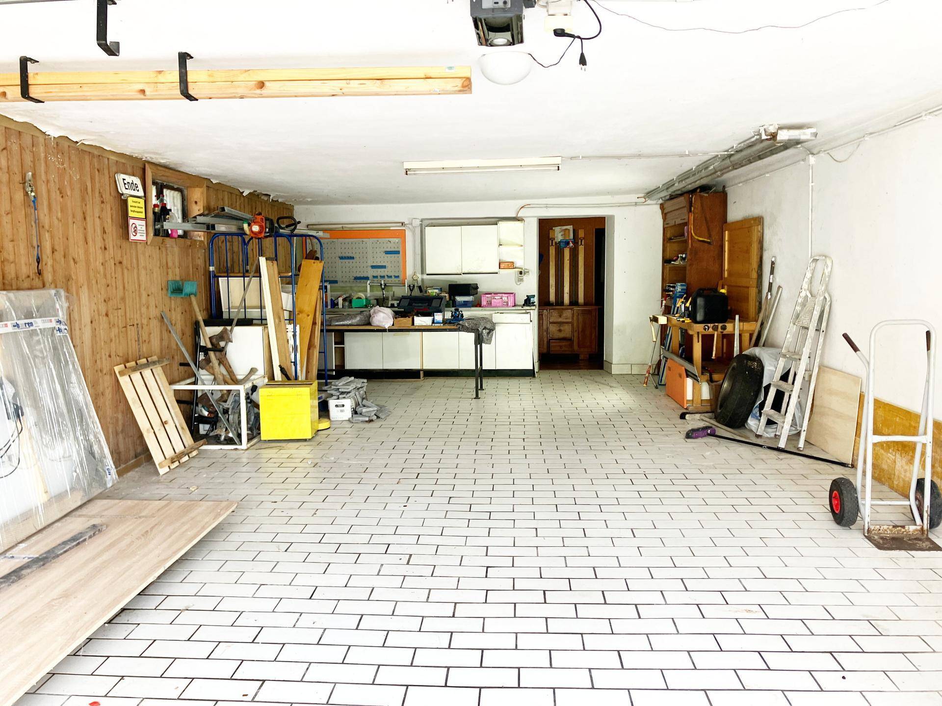 Geräumige Garage mit Werkstattbereich, gefliestem Boden und viel Stauraum für diverse Aktivitäten.