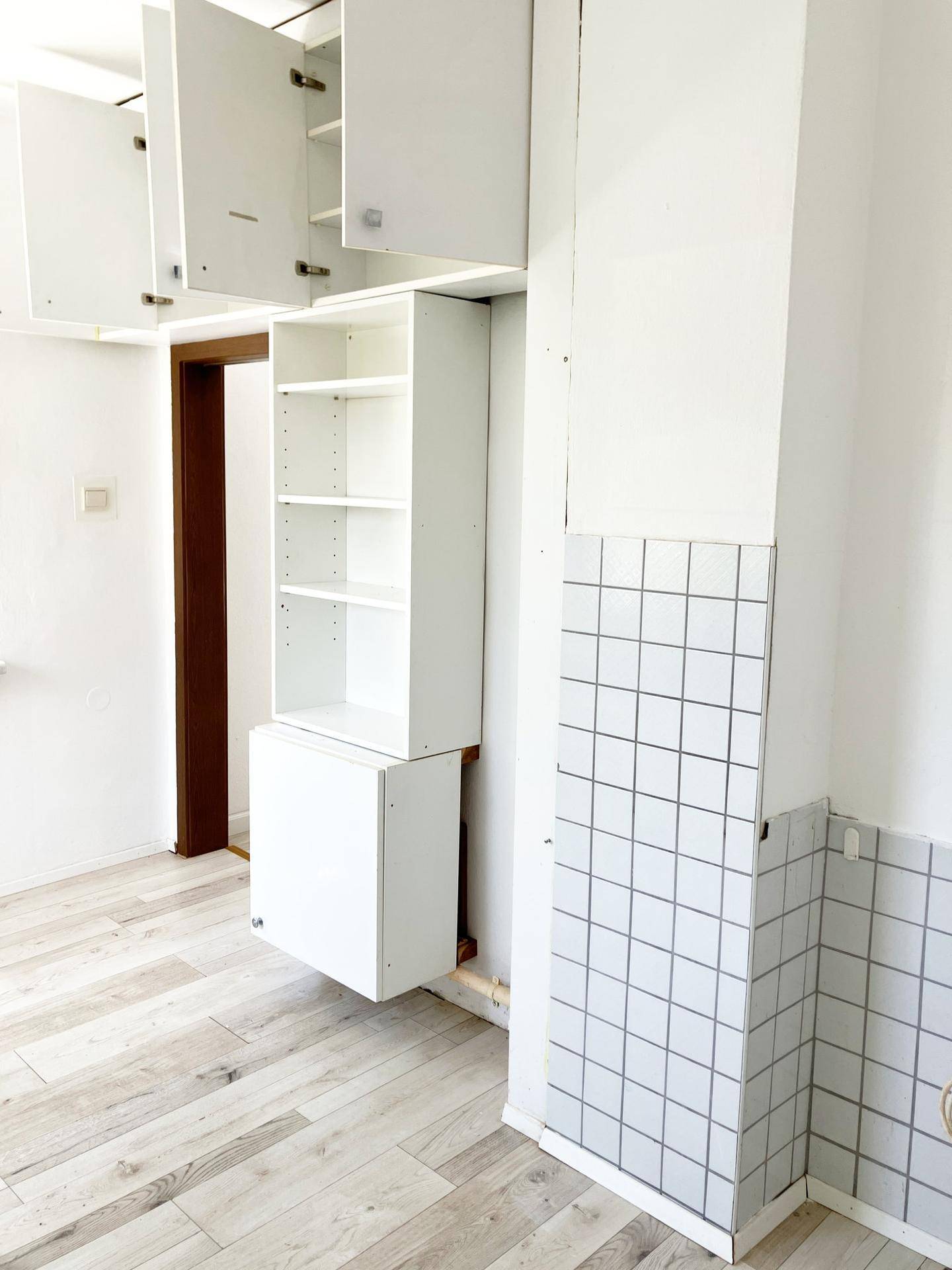 Ecke eines Raumes mit weißen Schränken und Regalen, ideal als Abstellraum oder kleine Küche.