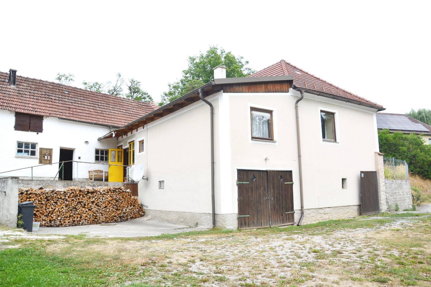 Seitenansicht des Hauses mit Holzstapel und Zufahrt.
