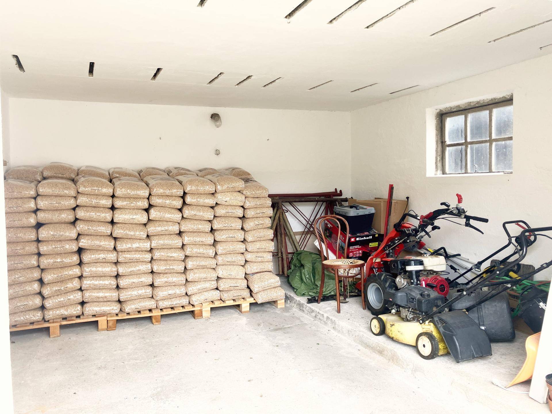 Geräumiger Lagerraum mit Holzpellets auf Paletten und verschiedenen Gartengeräten.