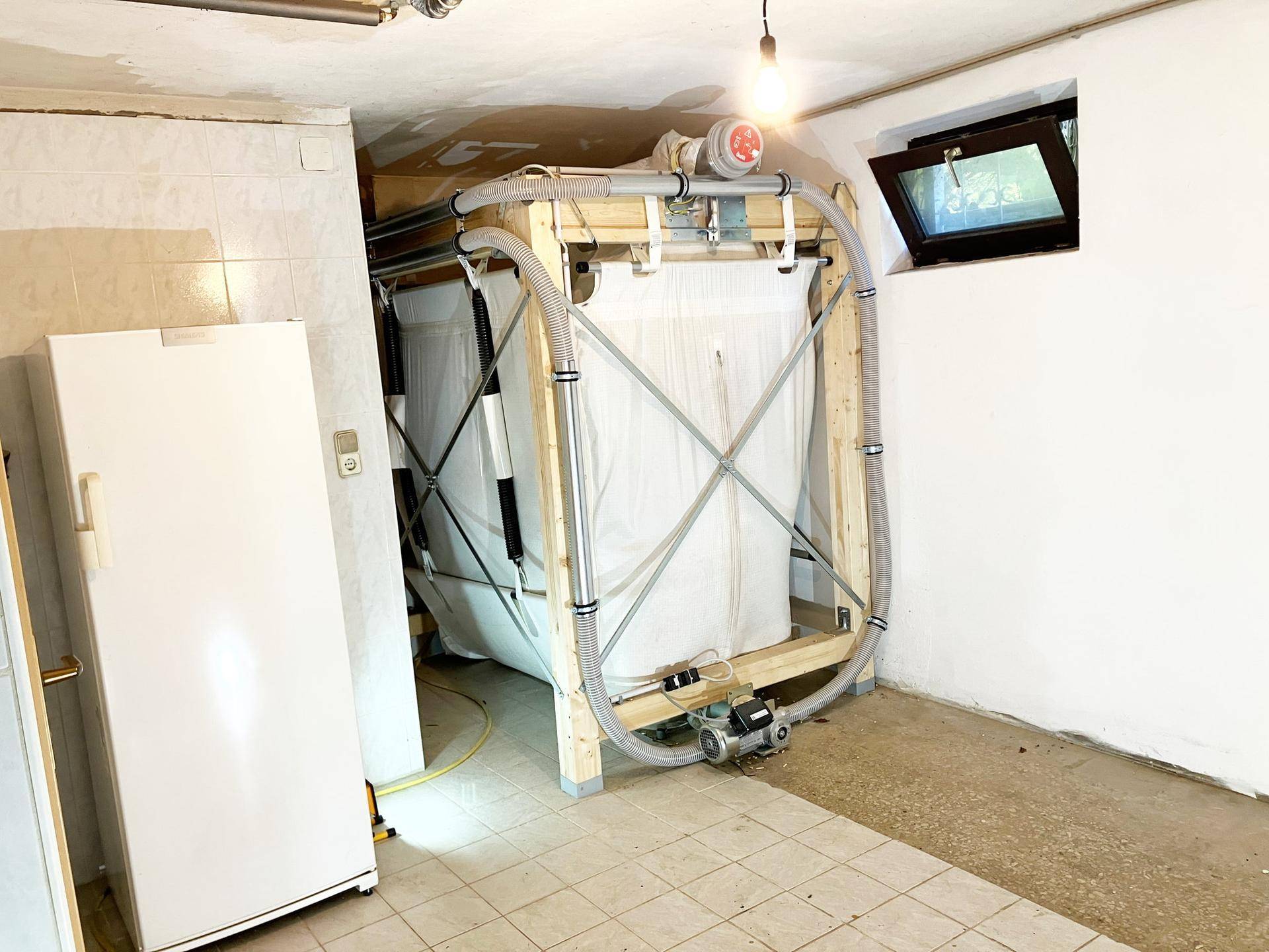 Kellerraum mit großem Lagerbehälter, einem Kühlschrank und einem kleinen Fenster.