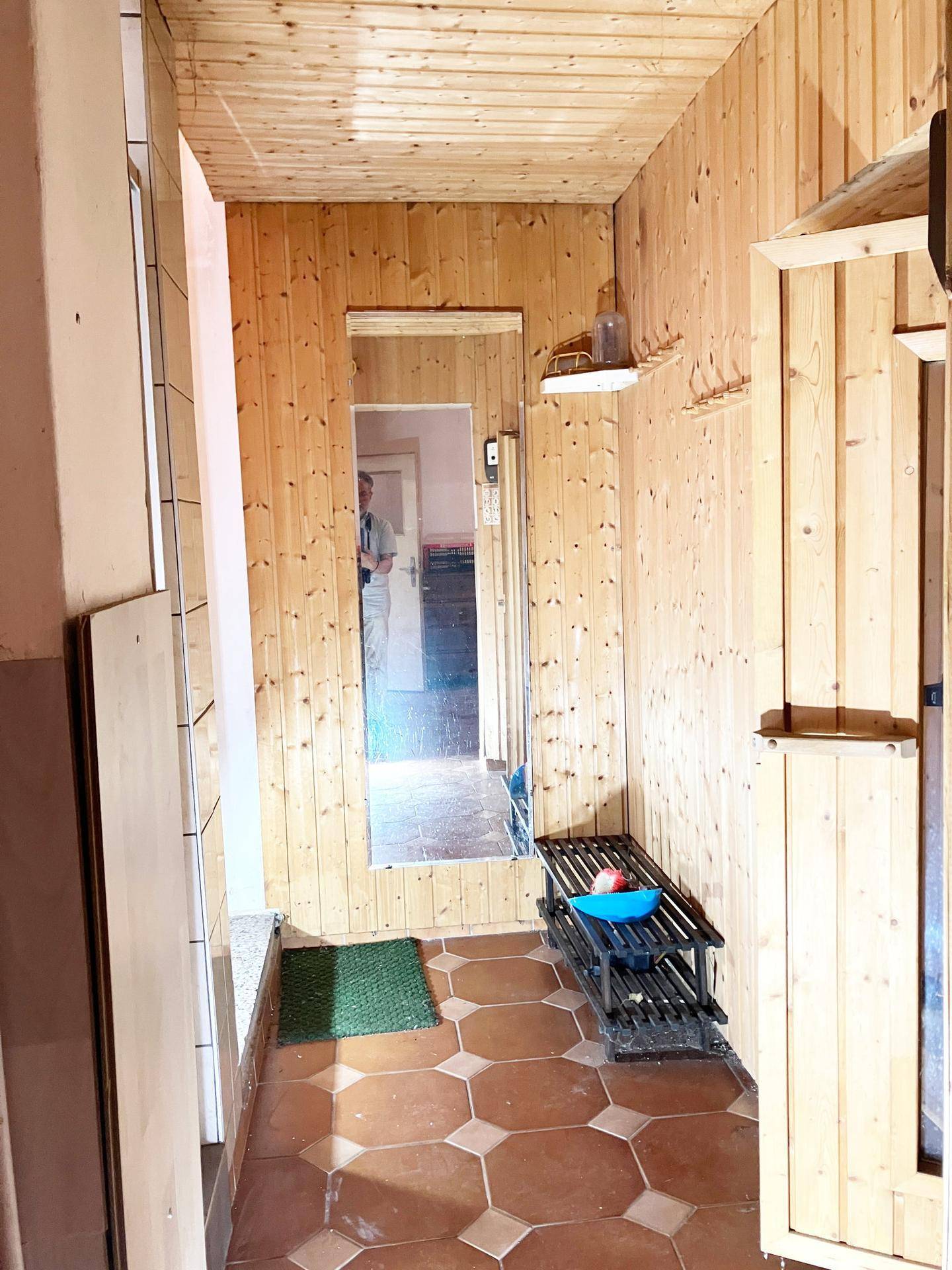 Holzvertäfelter Flur mit gefliestem Boden, Spiegel und Schuhregal.