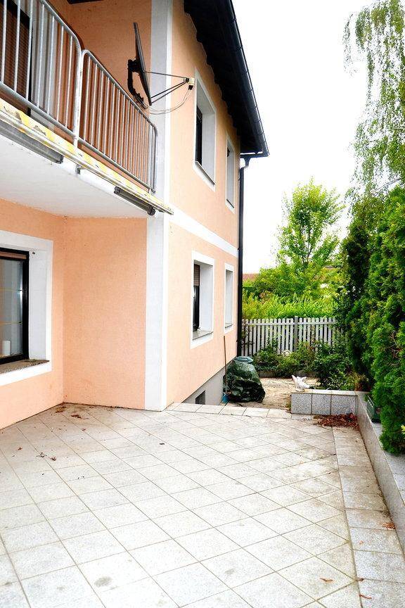 Geflieste Terrasse am Haus mit Blick auf den Garten und einem darüberliegenden Balkon.