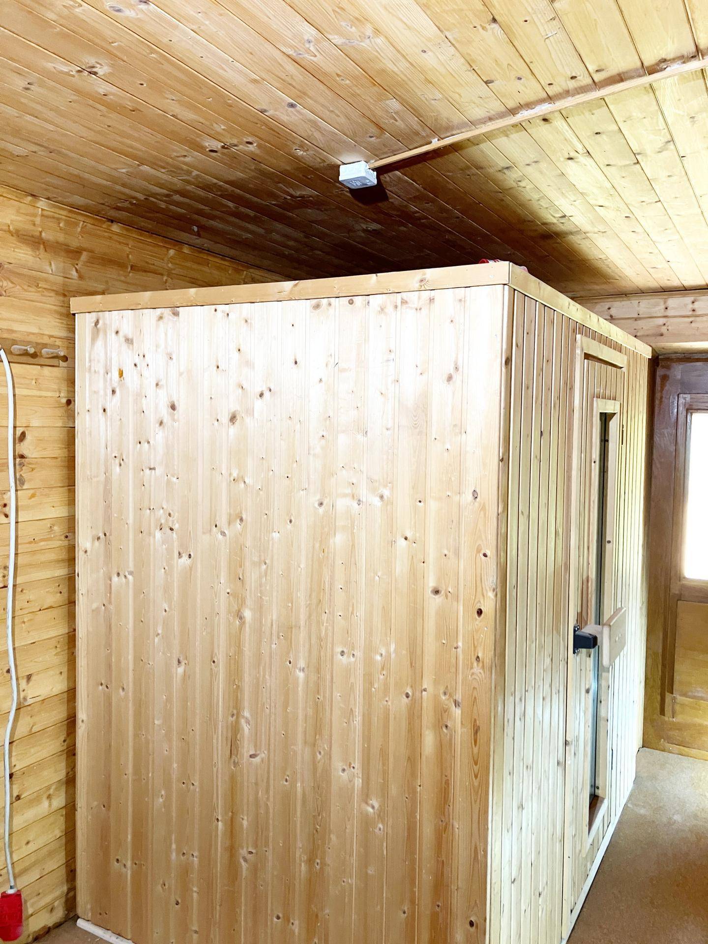 Raum mit einer freistehenden Saunakabine aus hellem Holz, umgeben von Holzverkleidung.