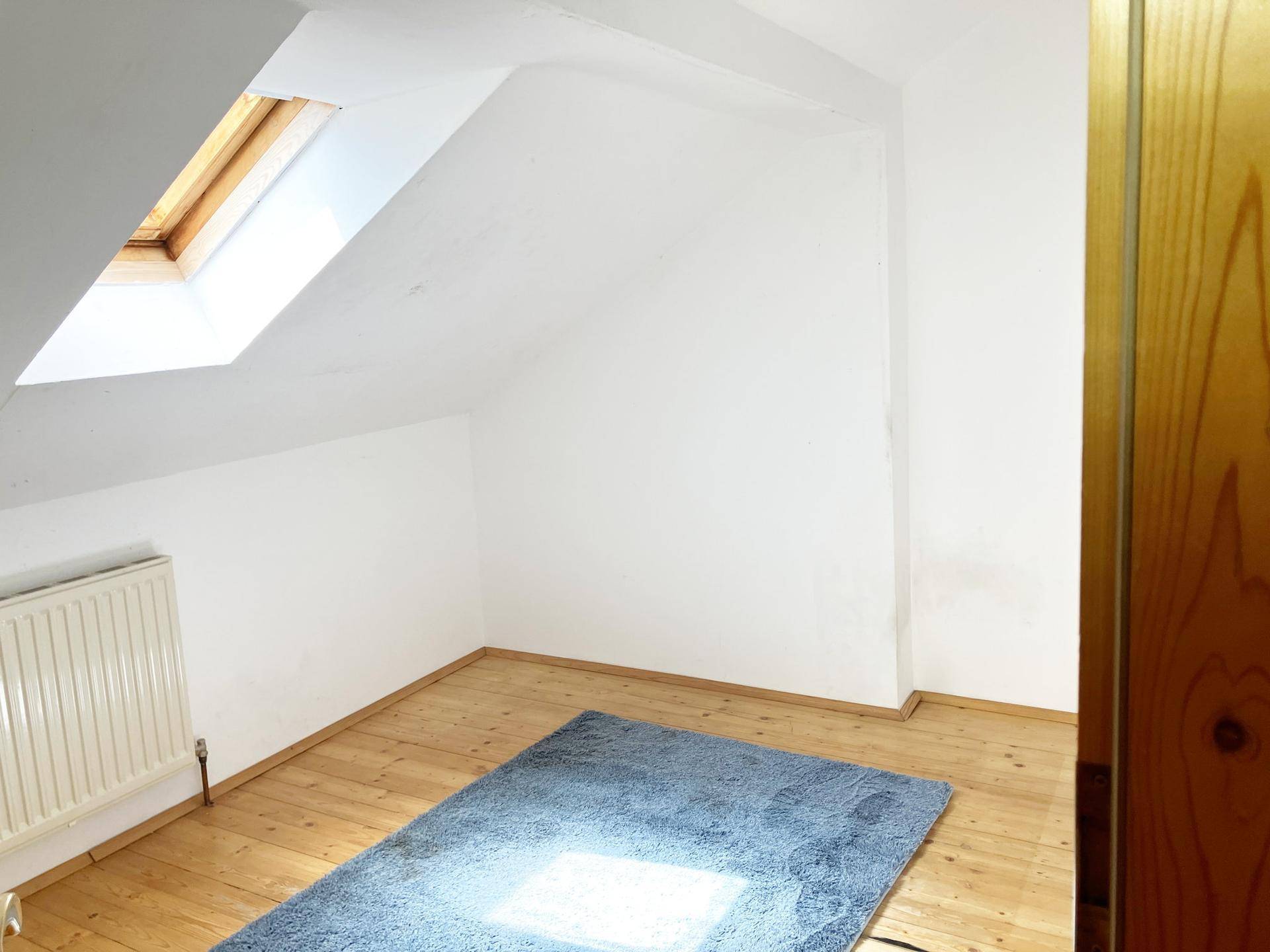 Dachzimmer mit Holzdielenboden, blauem Teppich und Dachfenster.