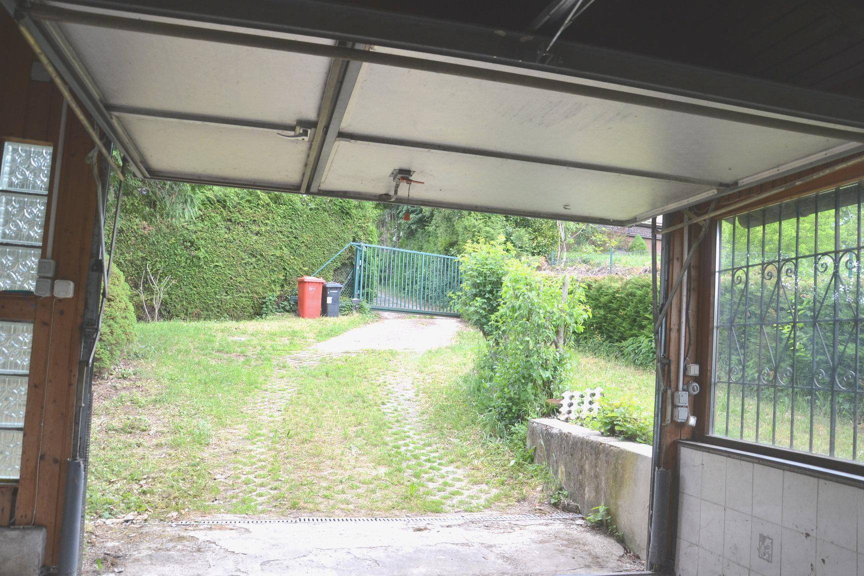 Blick aus der Garage auf eine gepflasterte Auffahrt und ein grünes Gartentor.