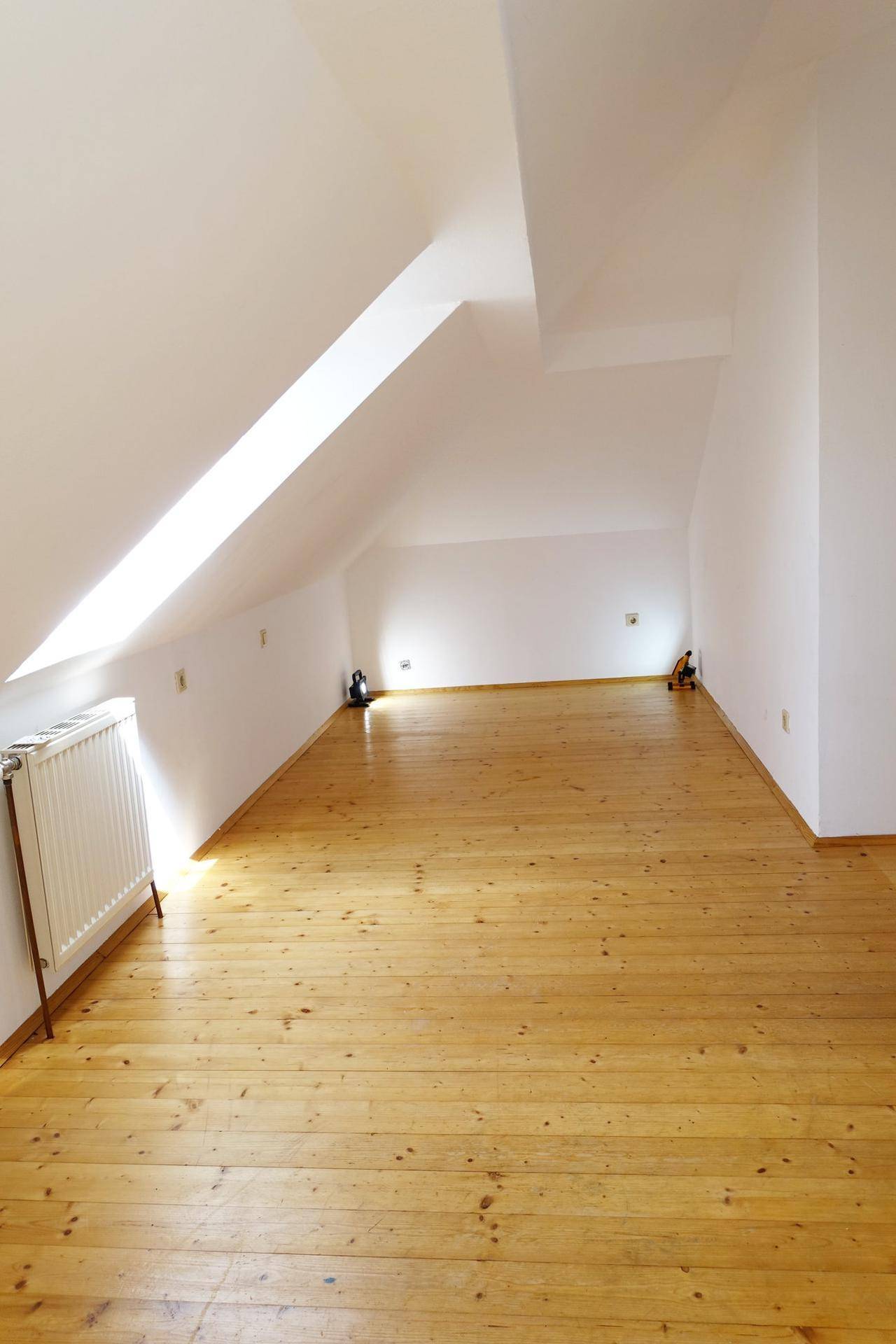 Helles Dachzimmer mit Holzdielenboden, schrägen Wänden und großem Dachfenster.
