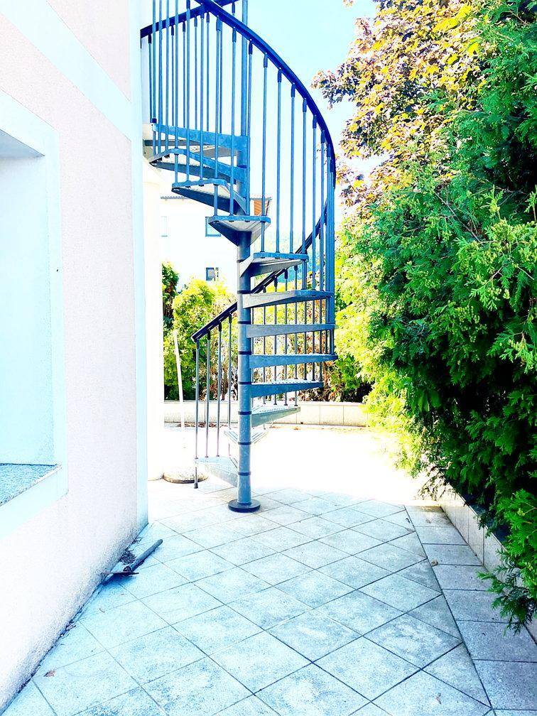 Blaue Wendeltreppe im Außenbereich, die eine Terrasse mit einer oberen Ebene verbindet.