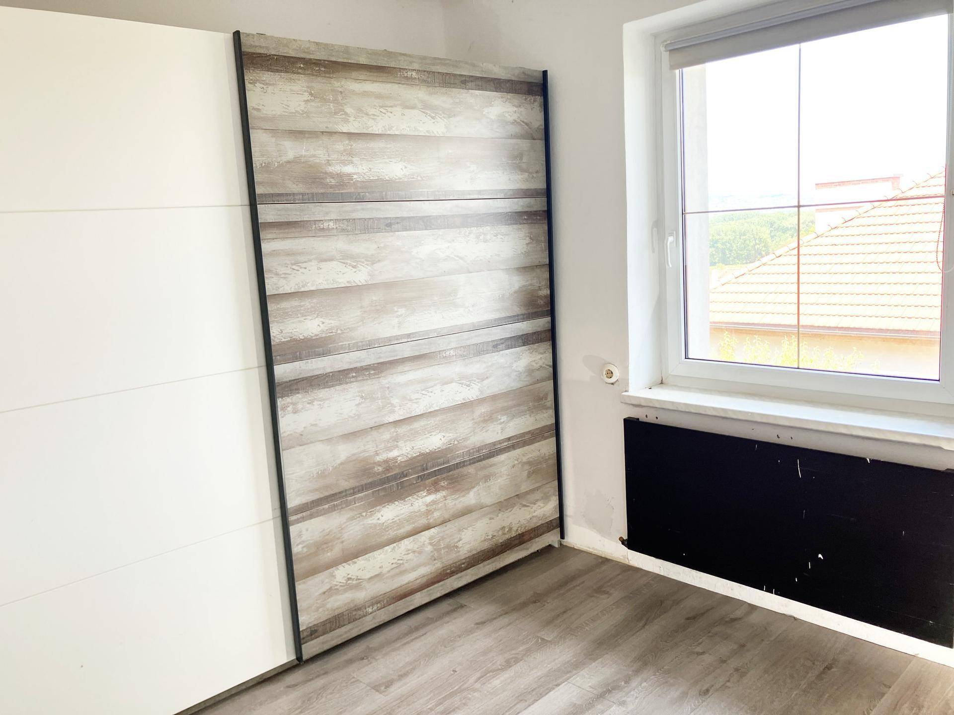 Helles Zimmer mit Holzboden, großem Fenster und integriertem Schrank mit Holzoptik.