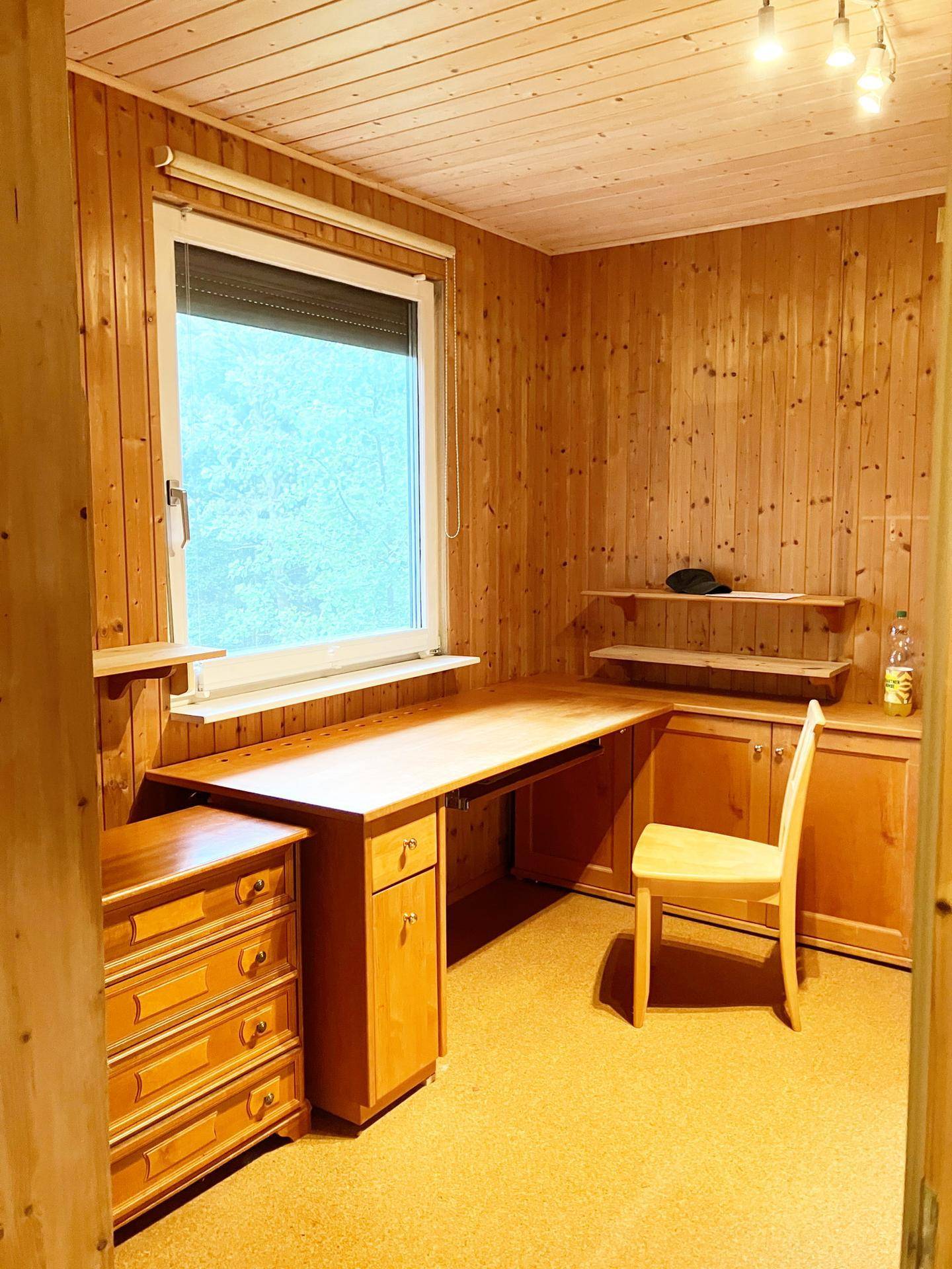 Arbeitszimmer mit Holzvertäfelung, Schreibtisch und Blick ins Grüne.