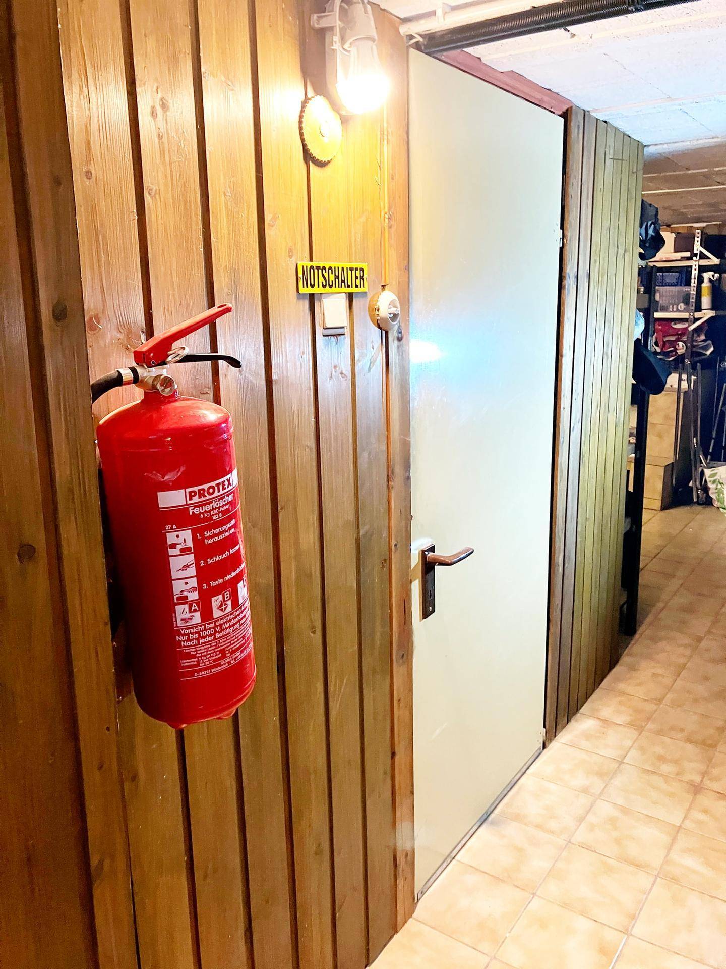 Abstellraum mit Holzverkleidung, Feuerlöscher und Notschalter, bietet Sicherheit und Stauraum.
