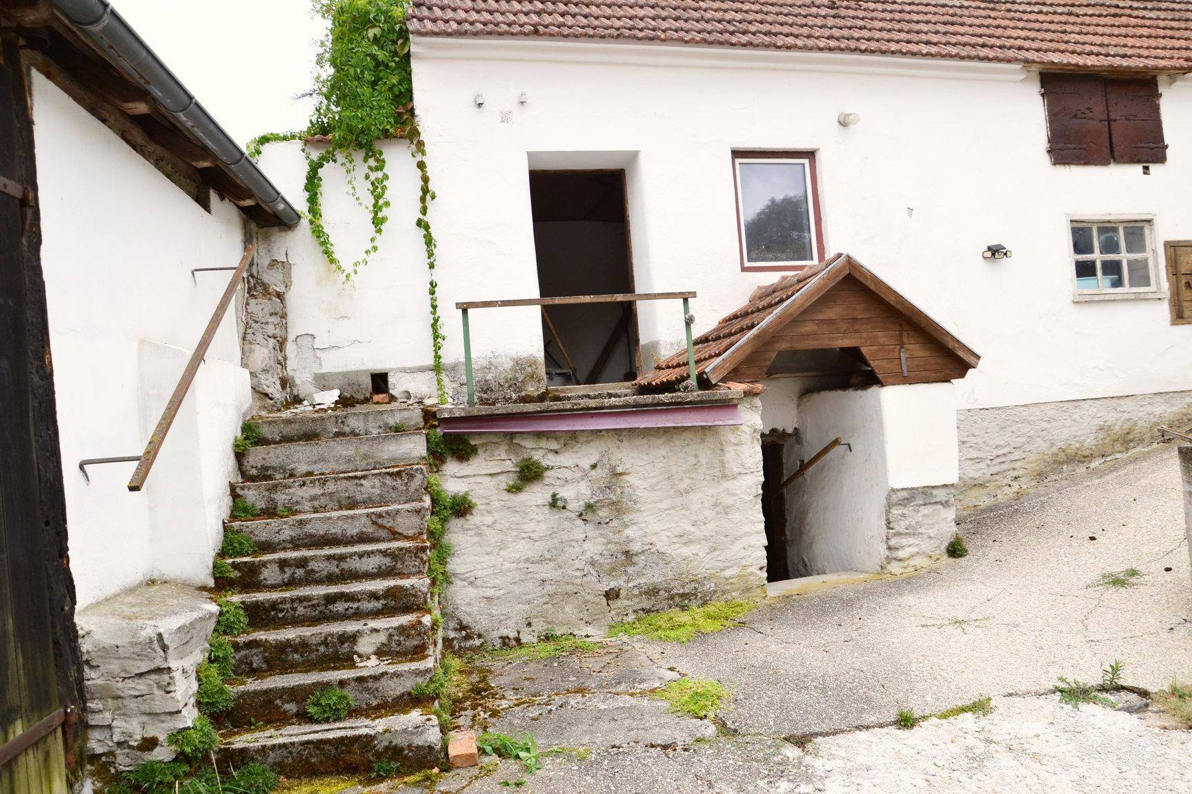 Außenansicht eines alten Gebäudes mit Steintreppen und einem überdachten Kellereingang.