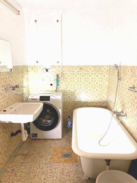 Badezimmer mit Badewanne, Waschbecken und Waschmaschine in älterem Zustand.