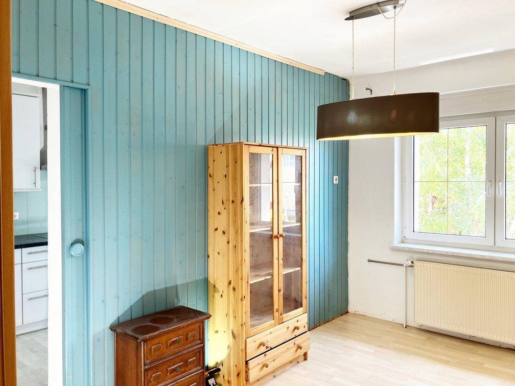 Raum mit blauer Holzvertäfelung, hellem Holzboden und einem Fenster, ideal als Wohnbereich.
