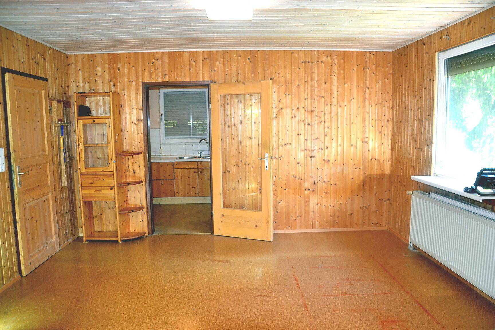 Geräumiger Wohnraum mit Holzvertäfelung und Blick in die angrenzende Küche.
