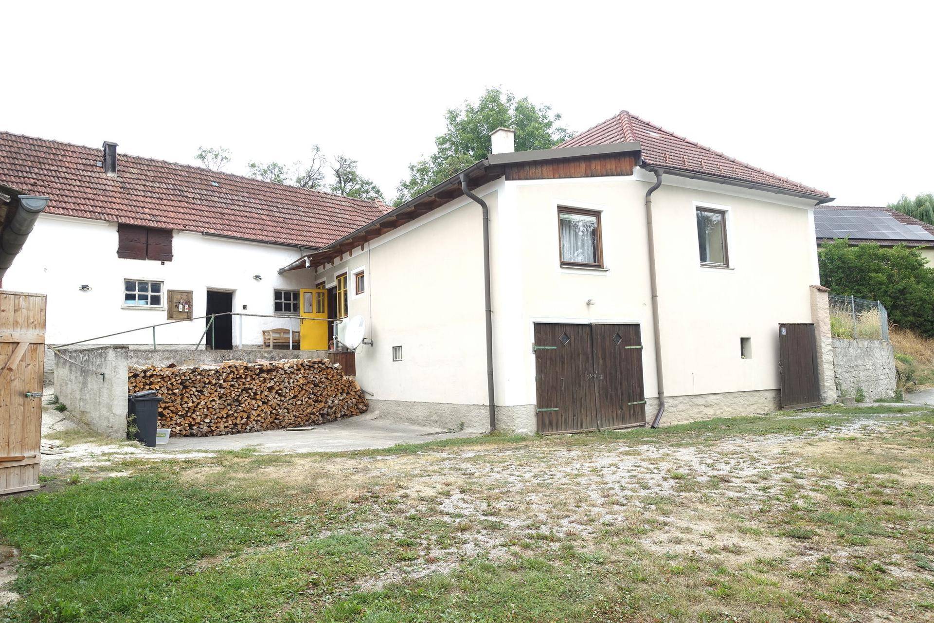 Seitenansicht des Anwesens mit Holzstapel und Zufahrtsbereich.
