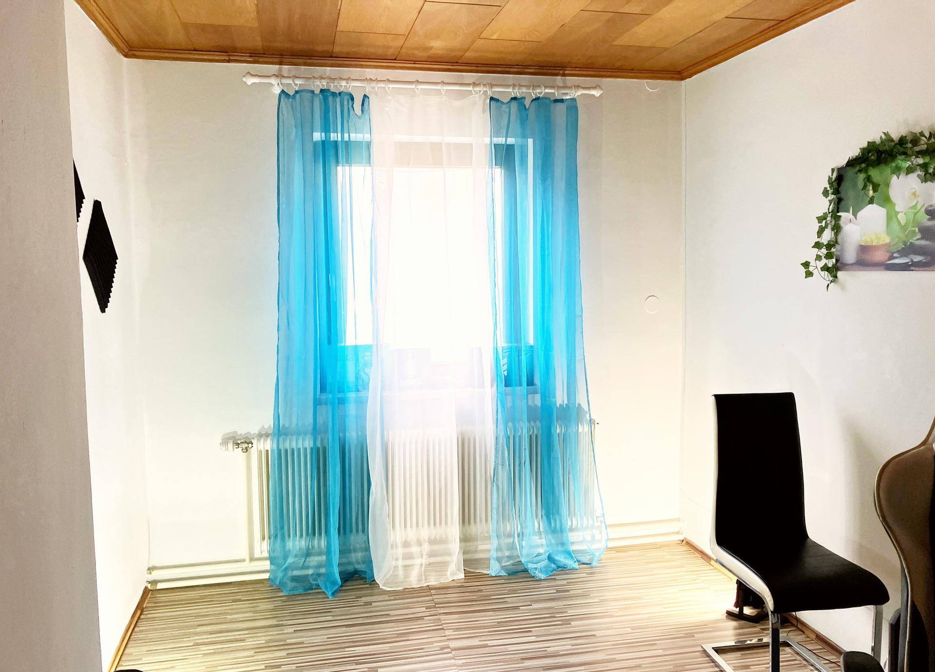 Helles Zimmer mit blauen Vorhängen, Holzdecke und Heizkörpern, bietet eine gemütliche Atmosphäre.