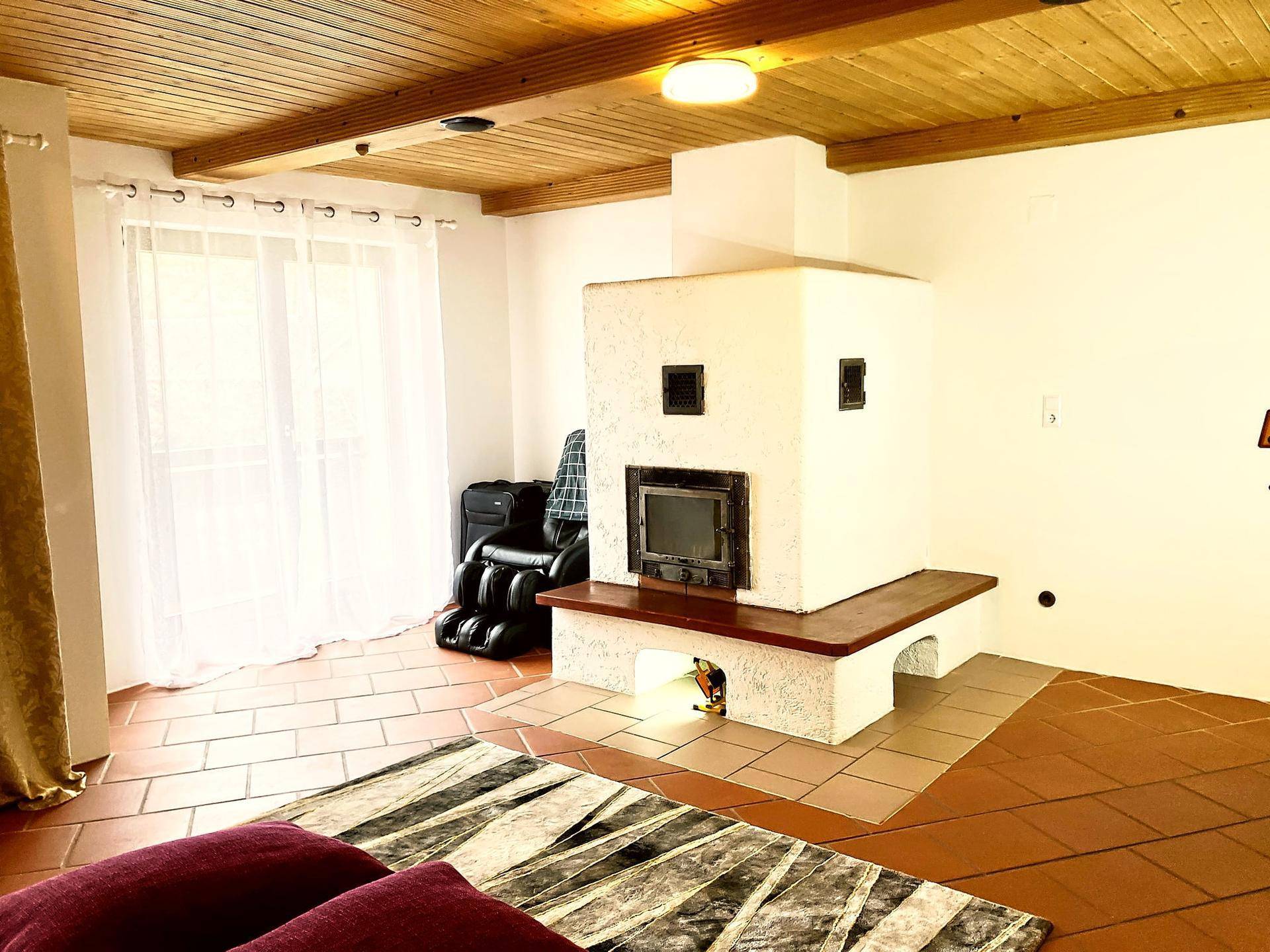 Wohnzimmer mit traditionellem Kachelofen, Terrakotta-Fliesenboden und Holzbalkendecke.