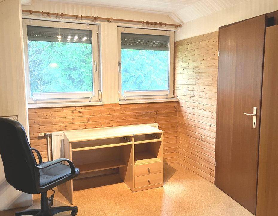 Schlafzimmer mit zwei Fenstern, Holzvertäfelung und Schreibtisch.