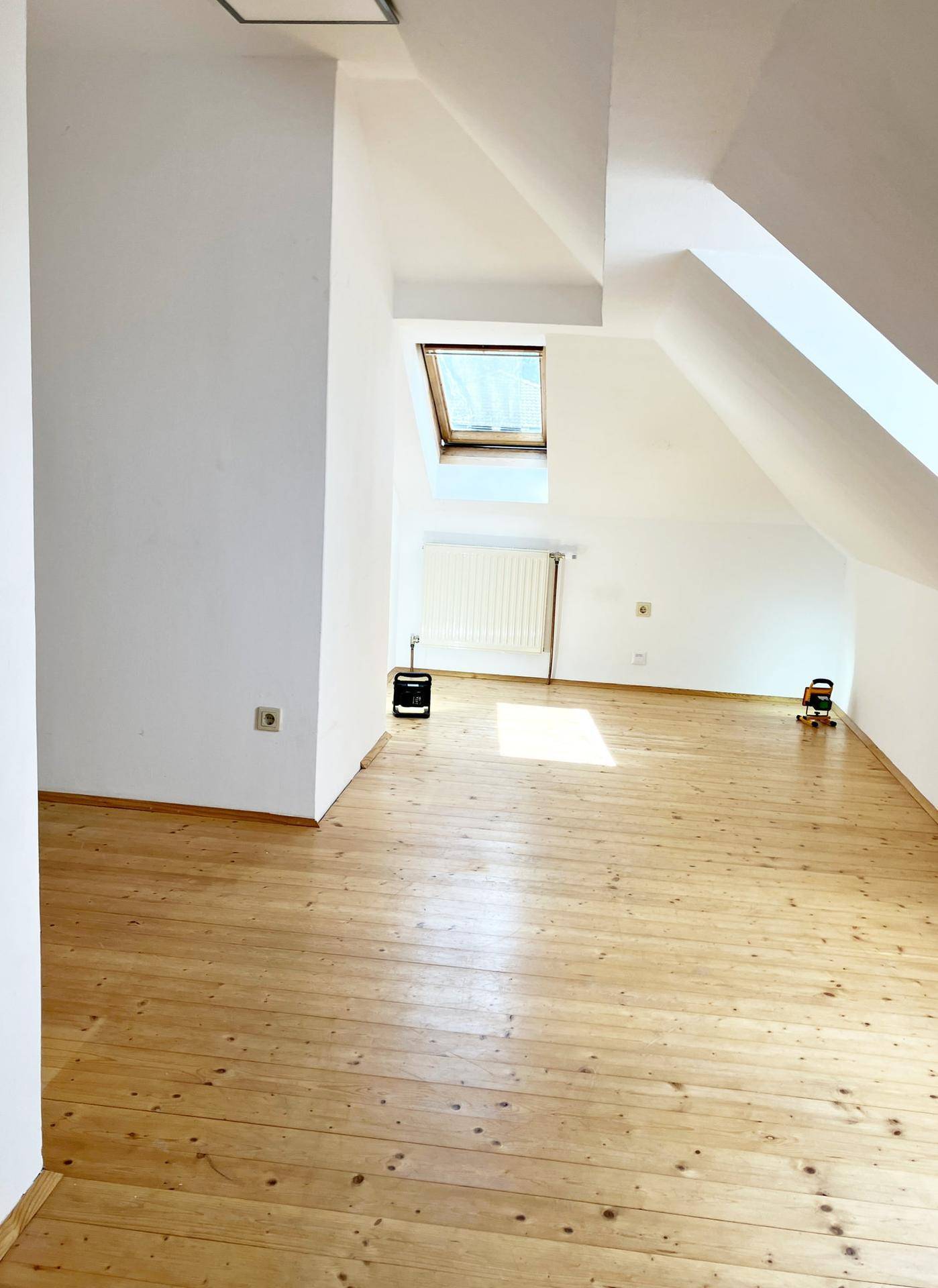 Geräumiges Dachzimmer mit Holzdielenboden, weiß gestrichenen Wänden und viel Tageslicht.