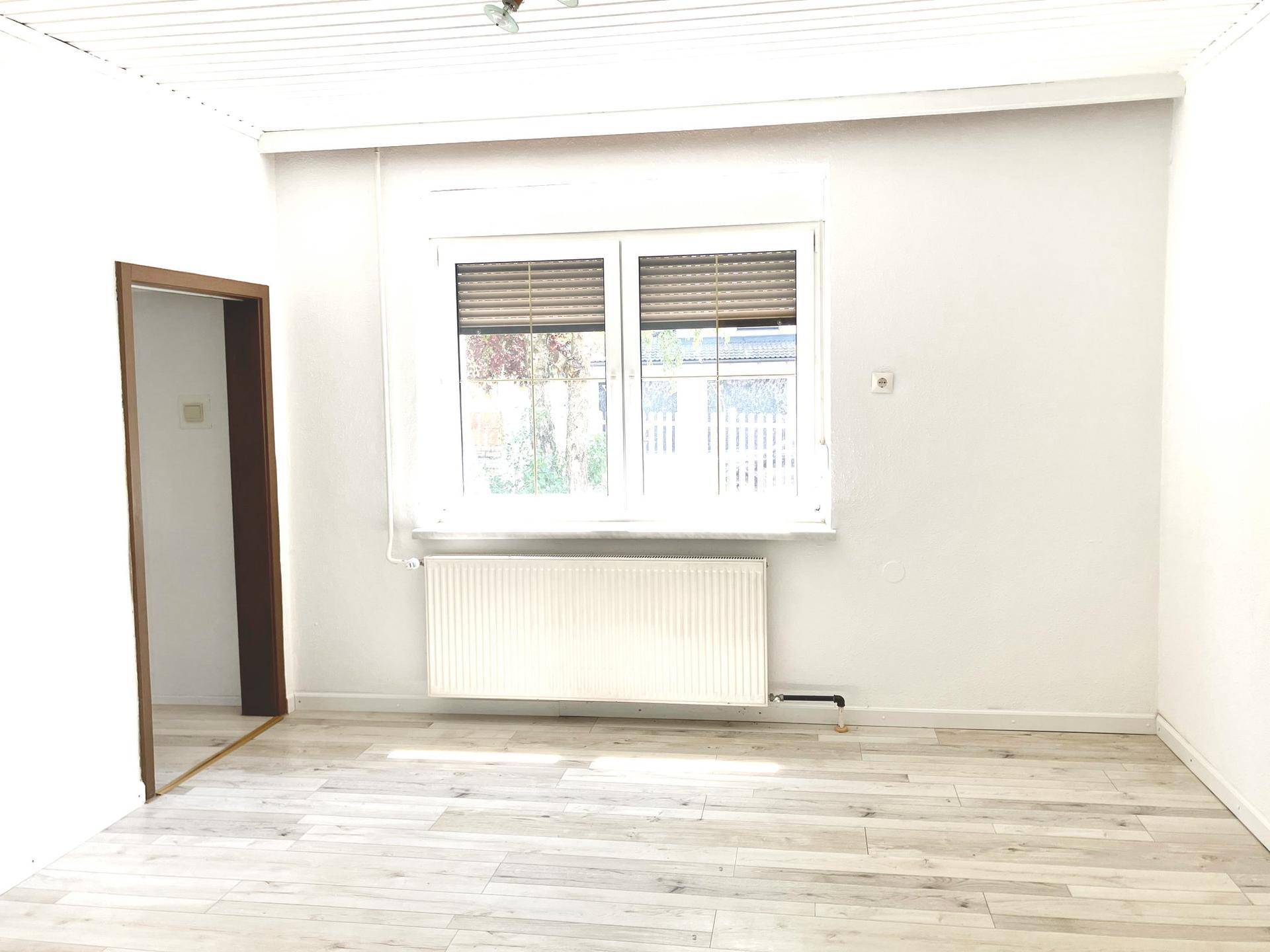 Heller Raum mit Laminatboden, großem Fenster und Heizkörper, bereit zur Einrichtung.