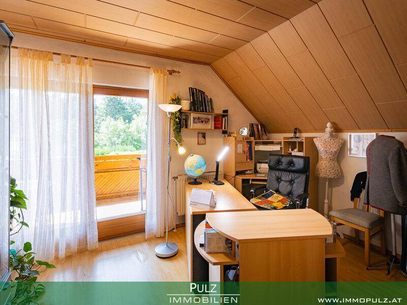 Helles Arbeitszimmer mit Dachschräge, Holztäfelung und Zugang zu einem Balkon.