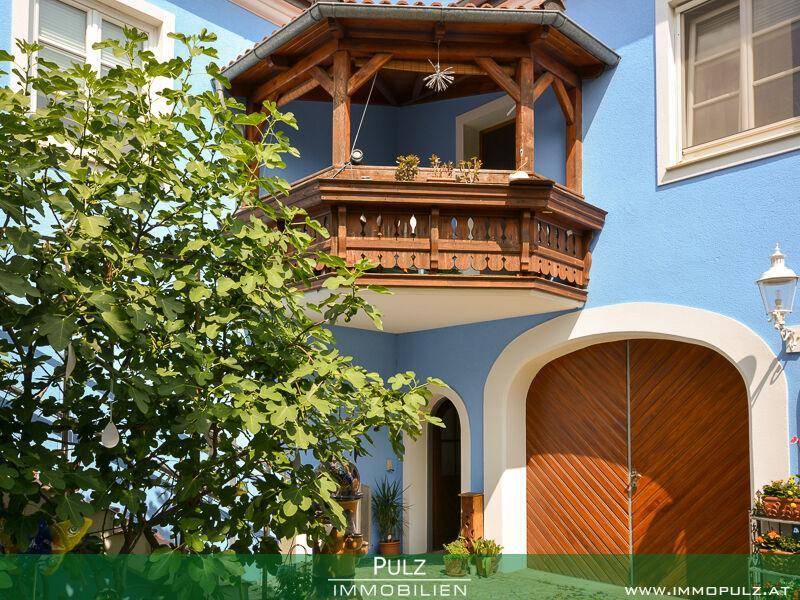 Traditioneller Holzbalkon mit kunstvollen Schnitzereien an einer blauen Hausfassade über einem Holztor.