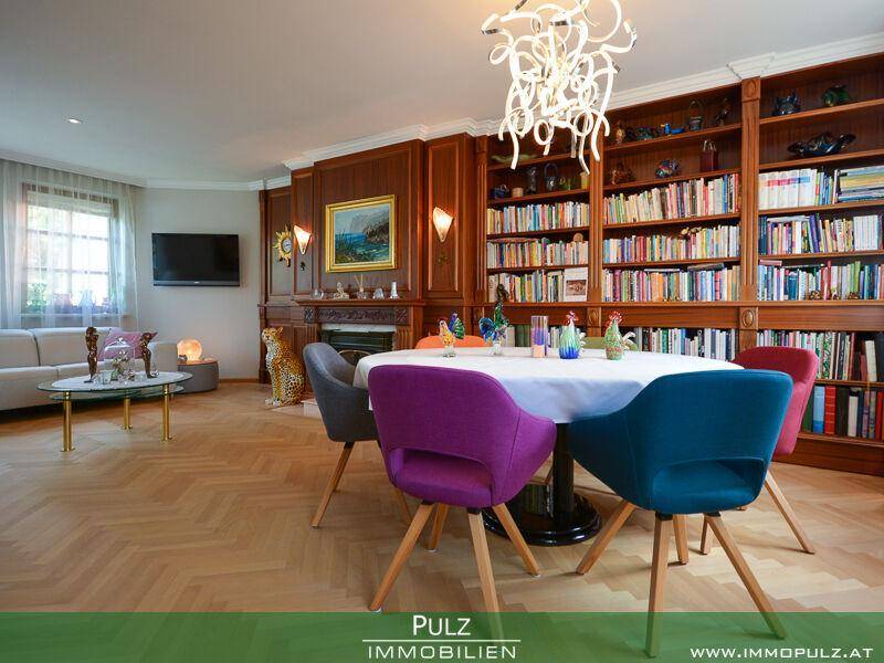 Eleganter Wohn-Essbereich mit Holzbücherregal, Parkettboden und farbenfrohen Stühlen am Esstisch.