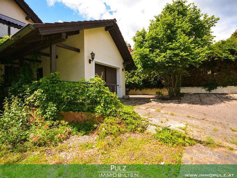 Seitenansicht des Hauses mit Garage, bewachsenem Eingangsbereich und Zufahrt.