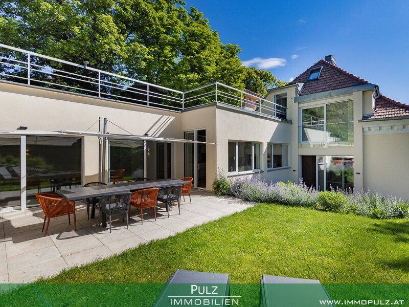 Weitläufige Terrasse mit Esstisch und Gartenmöbeln, angrenzend an einen gepflegten Rasen.