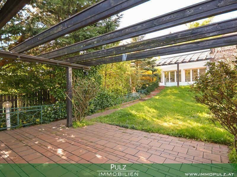Große gepflasterte Terrasse mit Holzpergola und Blick auf den Garten.