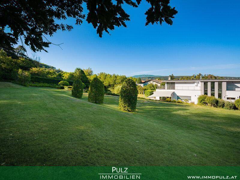 Weitläufige Rasenfläche mit gepflegten Sträuchern und Blick auf die moderne Architektur der Villa.