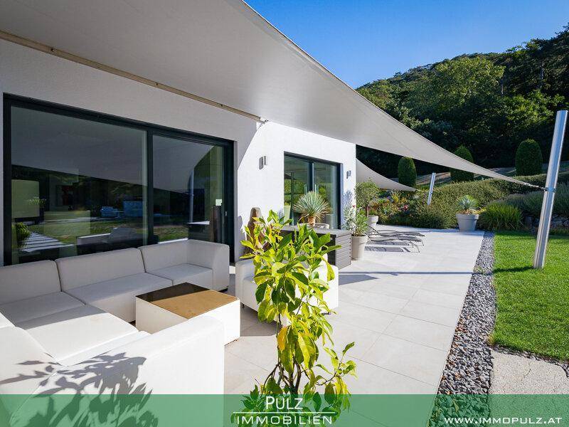 Helle Terrasse mit weißer Lounge-Möblierung, Sonnensegel und Blick auf den gepflegten Garten.