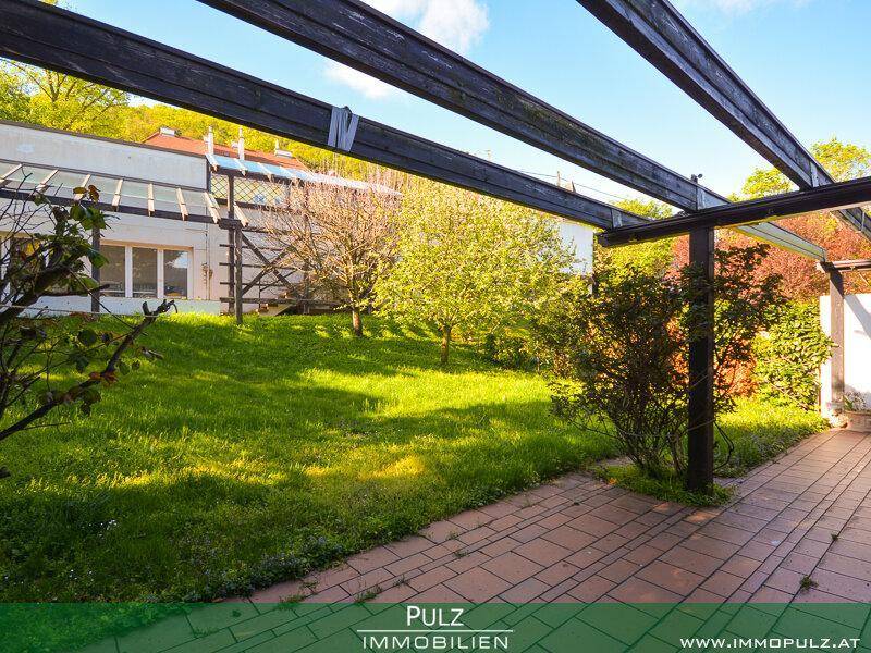 Sonnige Terrasse mit Pergola und weitläufigem Rasenbereich im Garten.