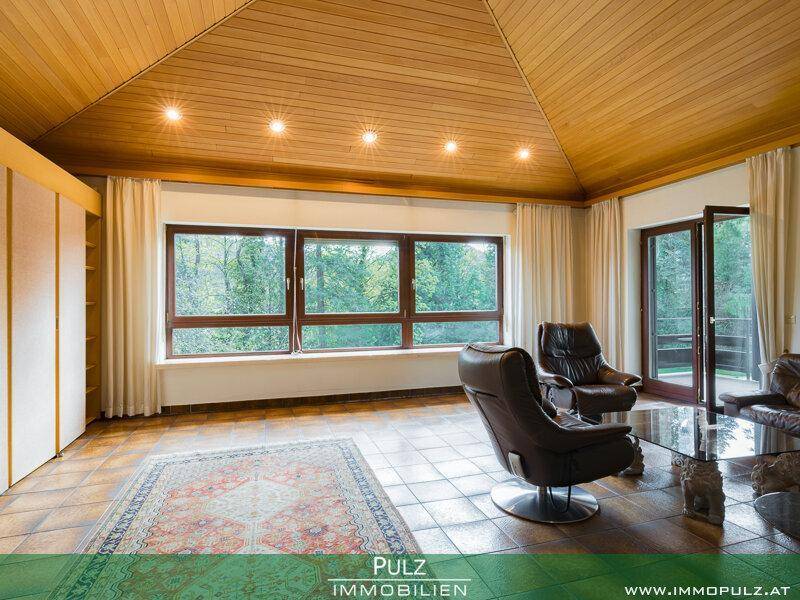 Geräumiges Wohnzimmer mit Holzdachschrägen, Fliesenboden und Panoramafenstern zum Garten.
