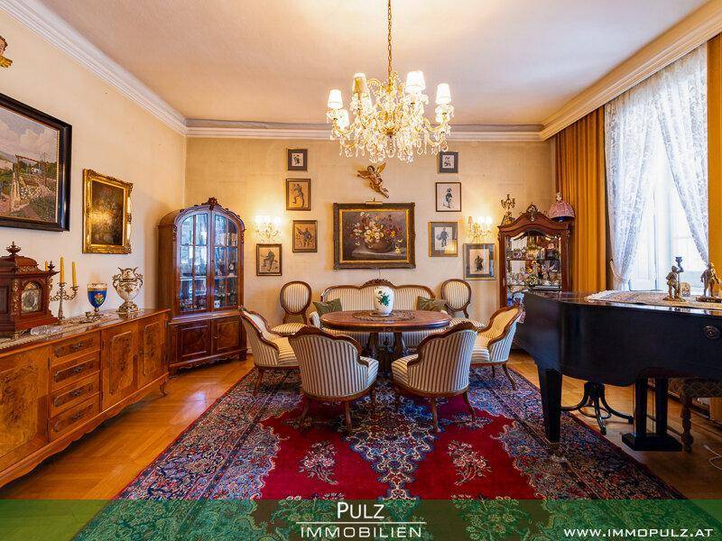 Elegantes Wohn- und Esszimmer mit antiken Möbeln, einem Flügel und einem prunkvollen Kronleuchter.