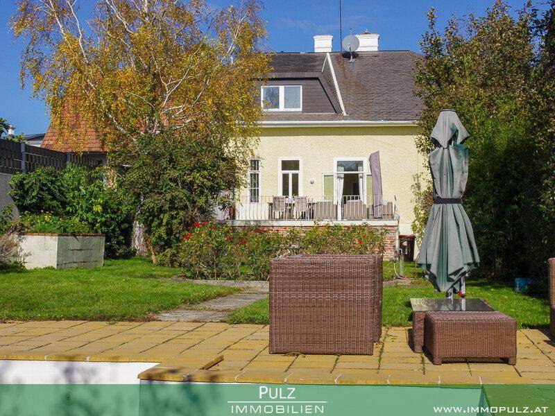 Rückansicht des Hauses mit großer Terrasse, Gartenmöbeln und gepflegtem Rasen.