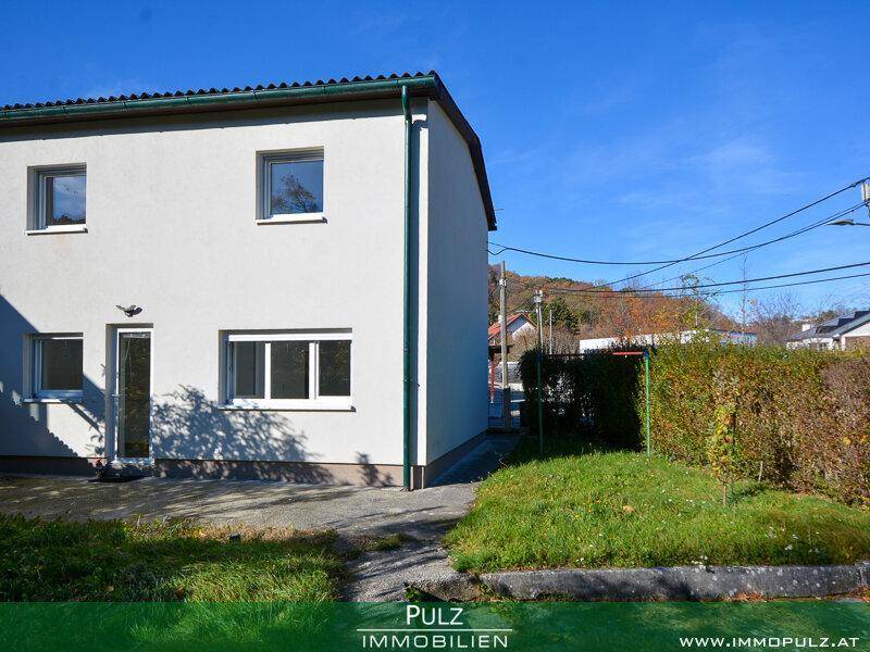 Seitenansicht des Hauses mit weißer Fassade und kleinem Rasenbereich.
