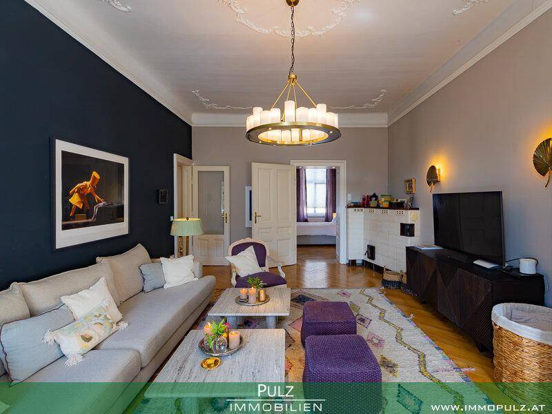 Helles Wohnzimmer mit Parkettboden, Kachelofen und modernem Sofa.